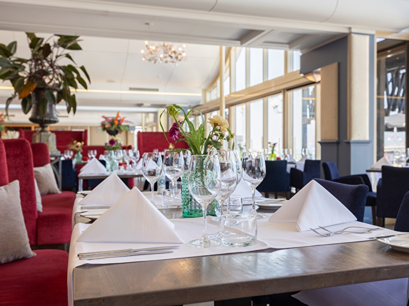 Restaurant Waves at the Kurhaus, met grote ramen en uitzicht op het water. Elegante tafels met witte linnen en bloemen.