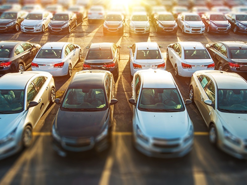 A parking lot with multiple rows of parked cars with the setting sun in the background