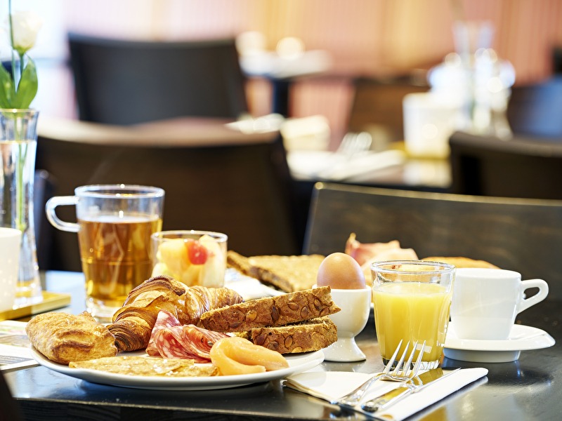 A breakfast plate with croissants, bread, cold cuts, salmon, a boiled egg, orange juice, and tea at Grand Hotel Amrâth Hotel Kurhaus
