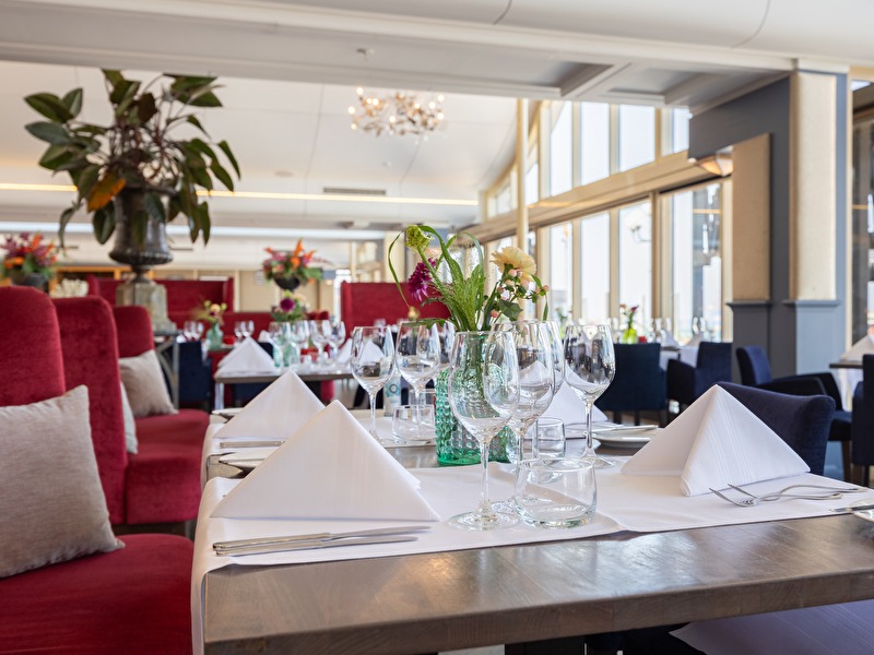 Table set with white linen, glass of water, and wine glasses on the table with luxurious red chairs at the Amrâth Kurhaus The Hague