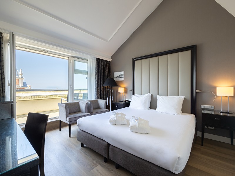 Executive kamer in Grand Hotel Amrâth Kurhaus met een tweepersoonsbed, twee grijze stoelen een bureau en uitzicht op zee